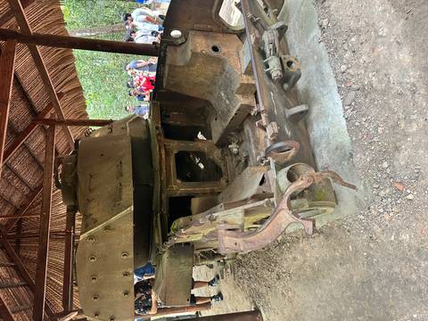       Rusty tank displayed outdoor with visitors around.
  