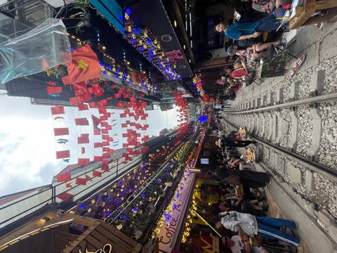 Vibrant street scene with colorful flags and bustling crowd along a railway.