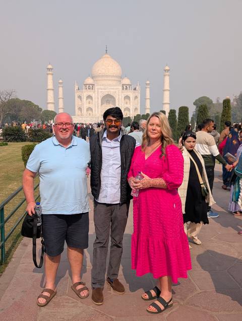Three people posing at the Taj Mahal with a crowd in the background.