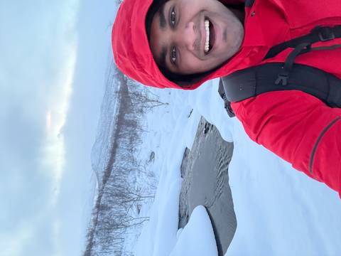 Person in a red jacket standing in a snowy landscape near a stream.