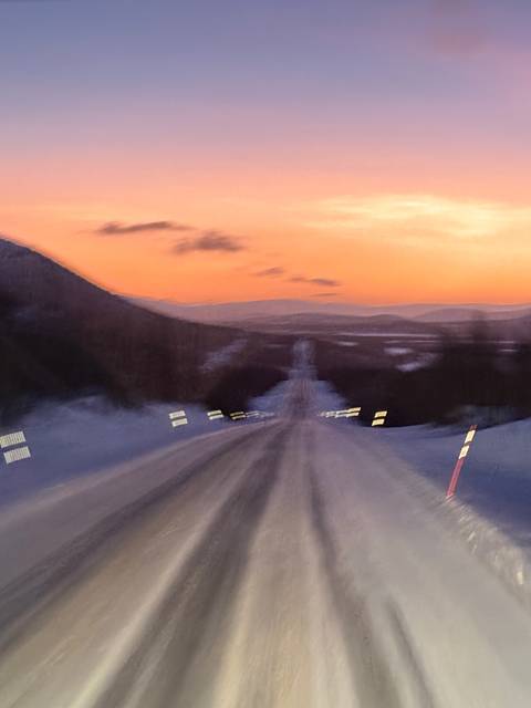 Blurry view of a snowy road at sunset.