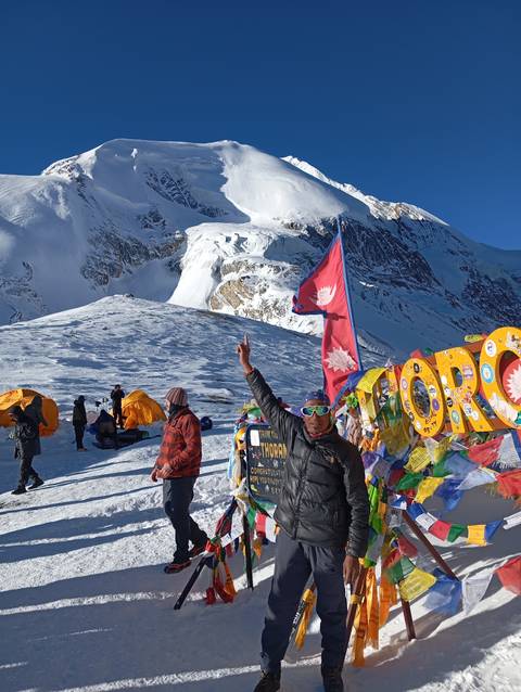      A person with a Nepalese flag, standing with mountains in view.
  