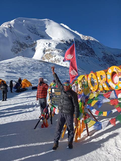       Two people standing by prayer flags with a snowy mountain in the background.
  