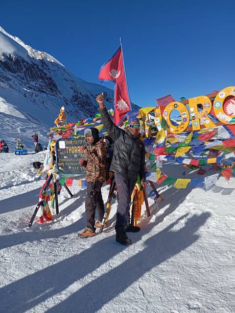       Two people standing at a snowy pass with celebratory flags.
  