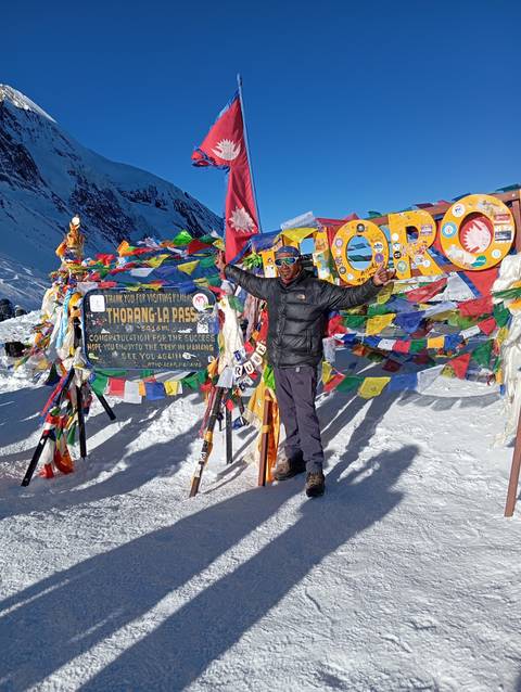       A lone trekker at a snowy pass with Nepalese flags.
  