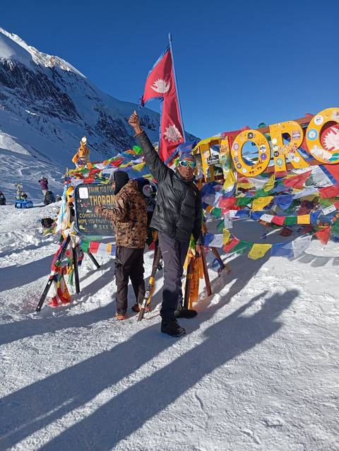       Two people at Thorong La Pass celebrating with colorful flags.
  