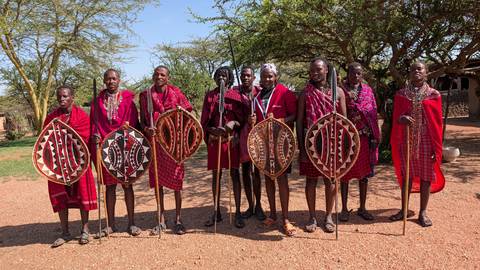 Group of Maasai people dressed in traditional attire holding shields.