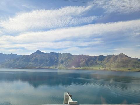 Mountain range reflecting on a calm lake under a partly cloudy sky.