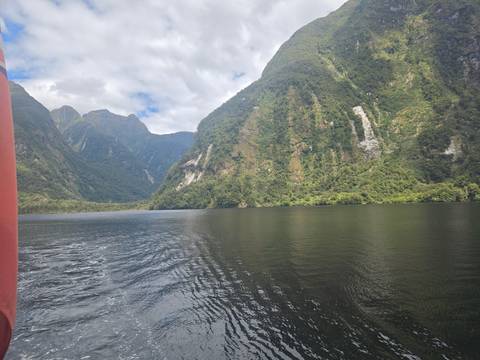 Lake surrounded by tall, forested cliffs under a partly cloudy sky.