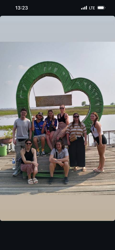       A group of people posing by a large decorative sign.
  