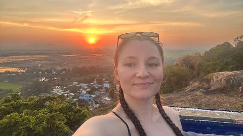 A woman taking a selfie at sunset overlooking a landscape.