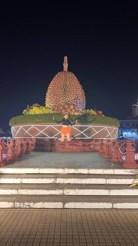 A person jumping in front of a large fruit sculpture at night.