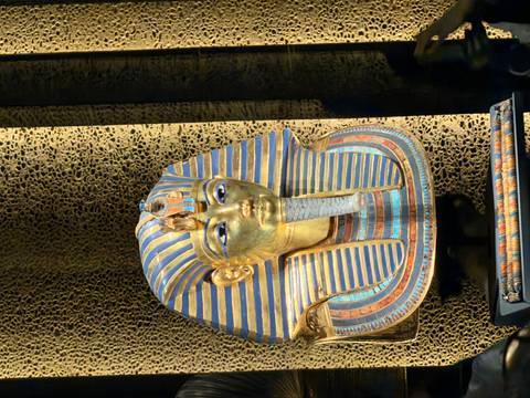 Golden pharaoh mask displayed in a museum setting.
