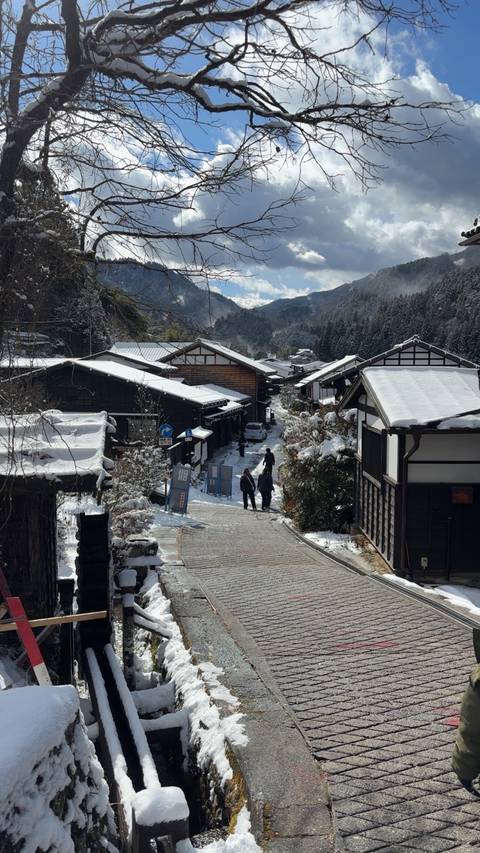       Two people walking down a snowy traditional Japanese street.
  