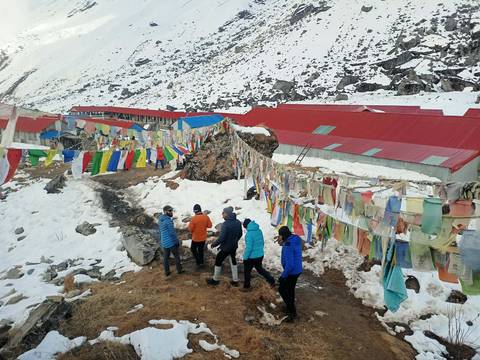       A group of hikers walking near colorful Buddhist prayer flags in a snowy landscape.
  
