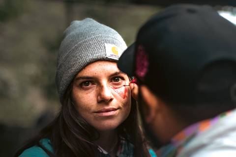       A person getting face paint from another person in a casual outdoor setting.
  