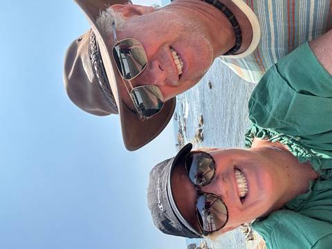       A couple smiling at the camera while standing near the ocean shore.
  