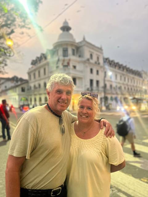 A couple posing in front of a historic building with blurred lights at dusk.
