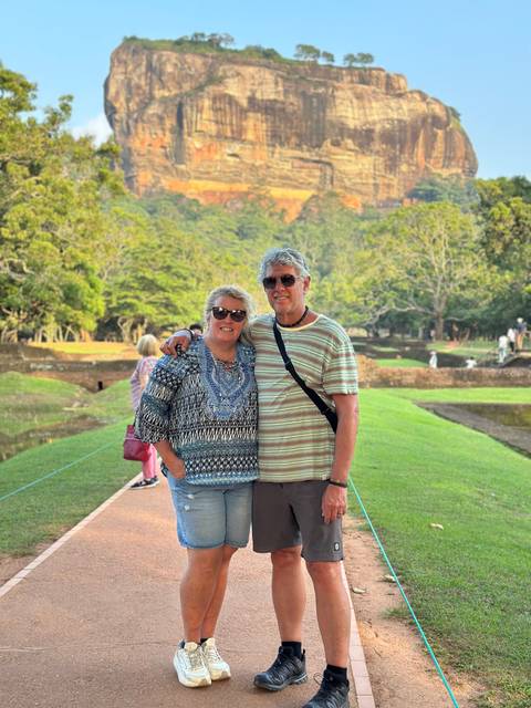 A couple posing in a manicured garden area with other tourists in the background.