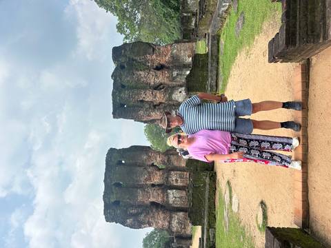 A couple posing in front of ancient ruins with partially rebuilt walls and structures.
