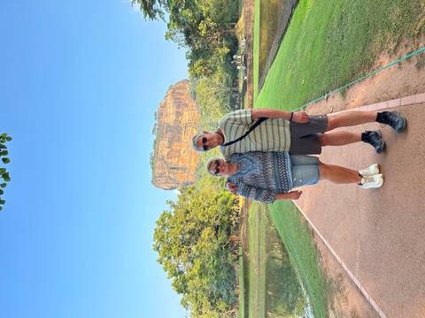       A couple posing with a view of a large rock formation rising above the landscape.
  