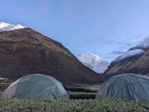      Two tents set in a mountainous landscape with snow-capped peaks under a clear sky.
  