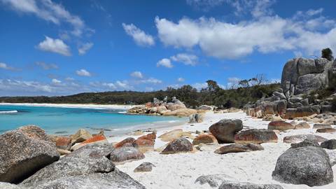       Rocks along a white sandy beach with clear blue waters under a sunny sky.
  