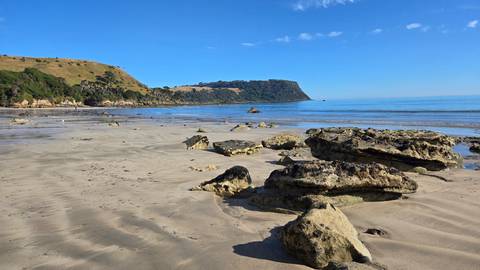 Sandy beach with rocky formations and hills in the background.