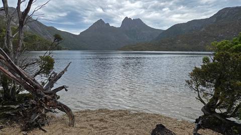       View from a lake shore looking at a mountain range under clouded skies.
  