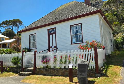       Small white house with flowers in front surrounded by a white picket fence.
  