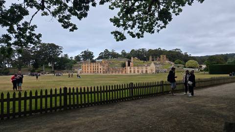       Ruined building with groups of people standing in an open field nearby.
  