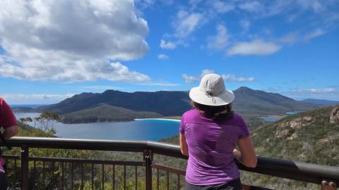Person enjoying the scenic view from a lookout over the ocean and mountains.