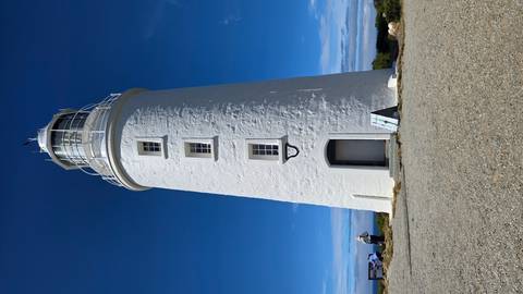       White lighthouse standing under a clear blue sky.
  
