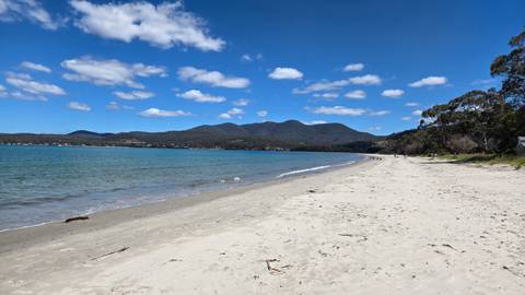      Empty sandy beach with clear blue skies and distant mountains.
  