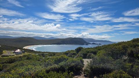       Panoramic view of a coastal area with lush greenery and vast ocean under blue skies.
  