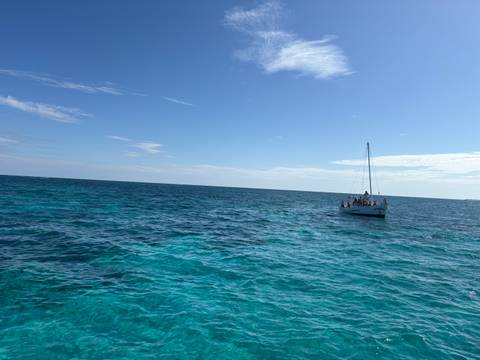 Sailboat on the ocean under a sunny sky with people on deck.