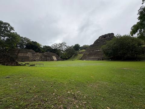 Ancient ruins in a grassy area surrounded by trees under cloudy skies.
