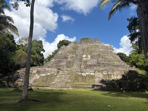 Stone pyramid ruin in a lush green area captured under a blue sky.