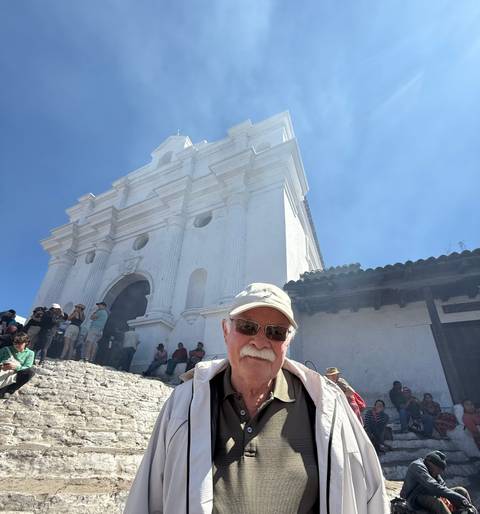       Group of tourists at a historical site, featuring a white cathedral.
  
