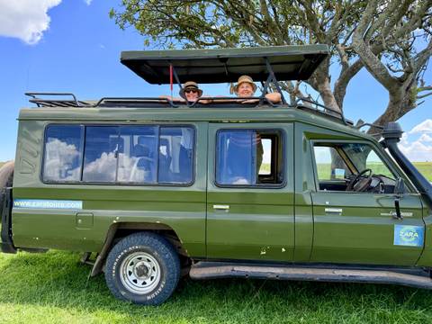 Two people in a safari vehicle in a green savannah landscape.