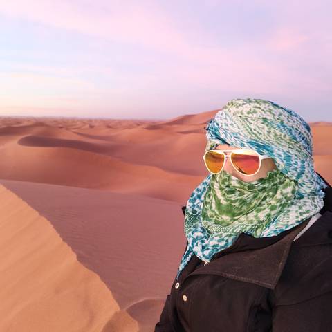       A person wearing a headscarf and sunglasses in the desert.
  
