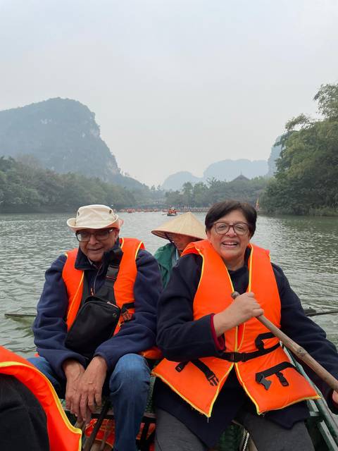 Elderly couple in life jackets on a boat in a scenic river setting.
