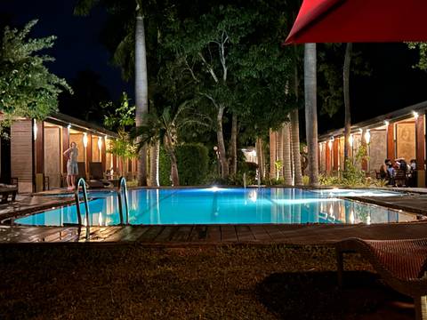 Outdoor swimming pool at night with people around and bungalows in the background