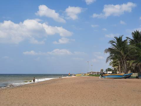       Sandy beach with boats and a person walking along the shore
  
