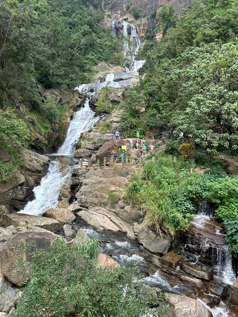Waterfall surrounded by greenery with tourists on the bridge
