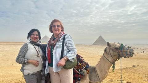 Two women with a camel posing in front of pyramids in Giza, Egypt.