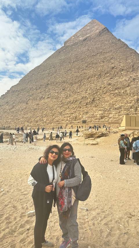 Two women standing against a pyramid background with many visitors around in Giza, Egypt.