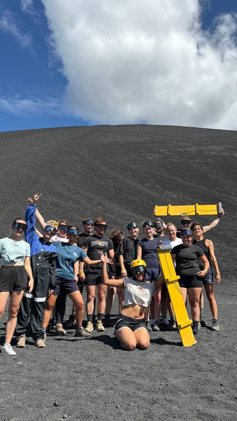       Group posing on a volcanic ash surface with goggles and sandboards.
  
