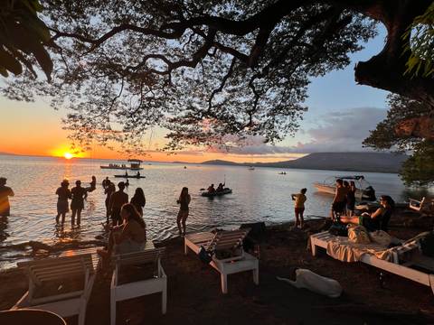       People enjoying a lakeside sunset with boats.
  