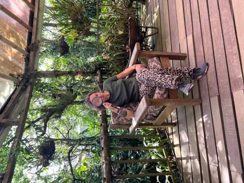       Person sitting on a wooden porch surrounded by plants holding a magnifying glass.
  